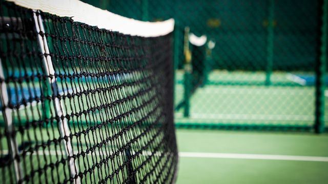 An empty pickleball court with a white net on a green surface