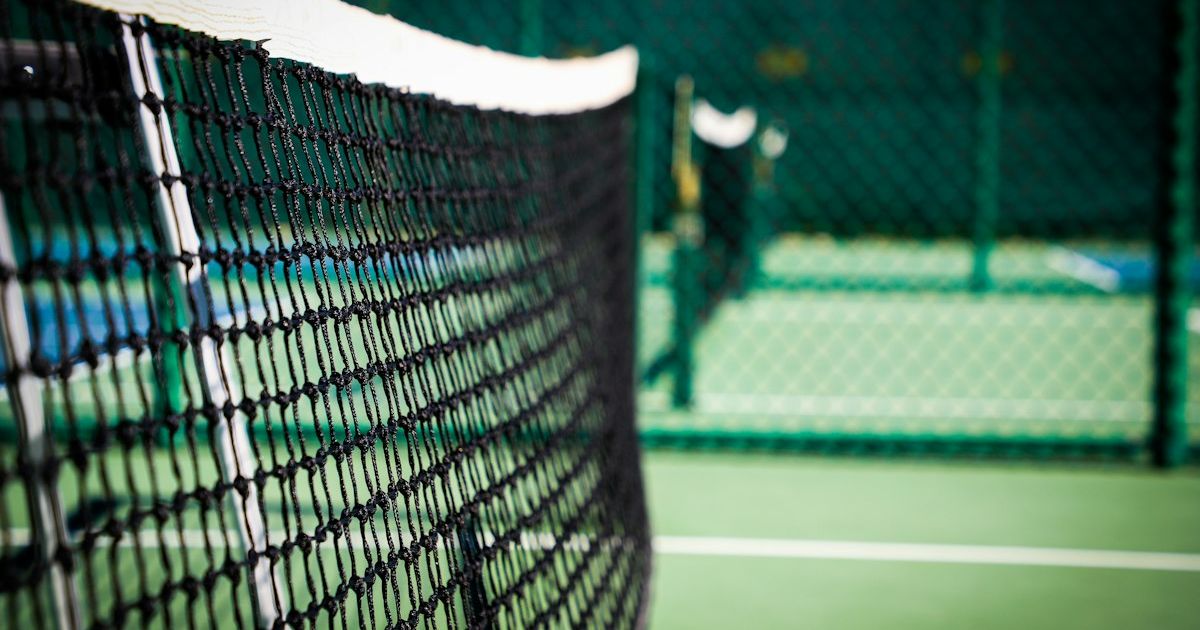 An empty pickleball court with a white net on a green surface