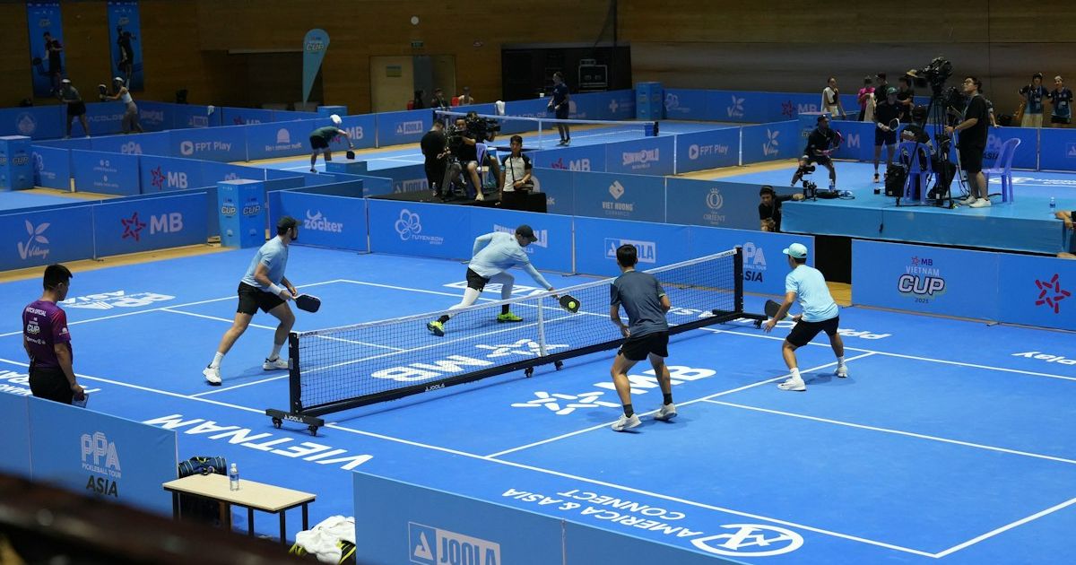 Players competing with paddles and a yellow pickleball on a blue outdoor court