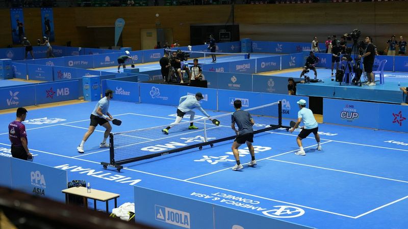 Players competing with paddles and a yellow pickleball on a blue outdoor court